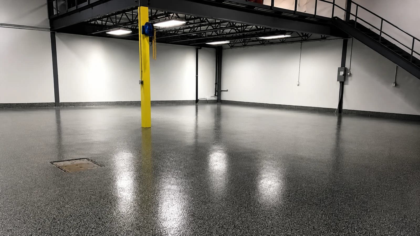 Flake epoxy floor under a steel mezzanine in a plant, reflecting the overhead lights