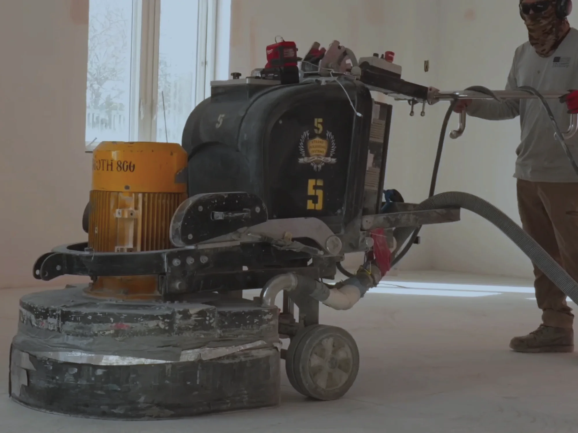 Crew member running a floor grinder with its dust extraction hose and vacuum