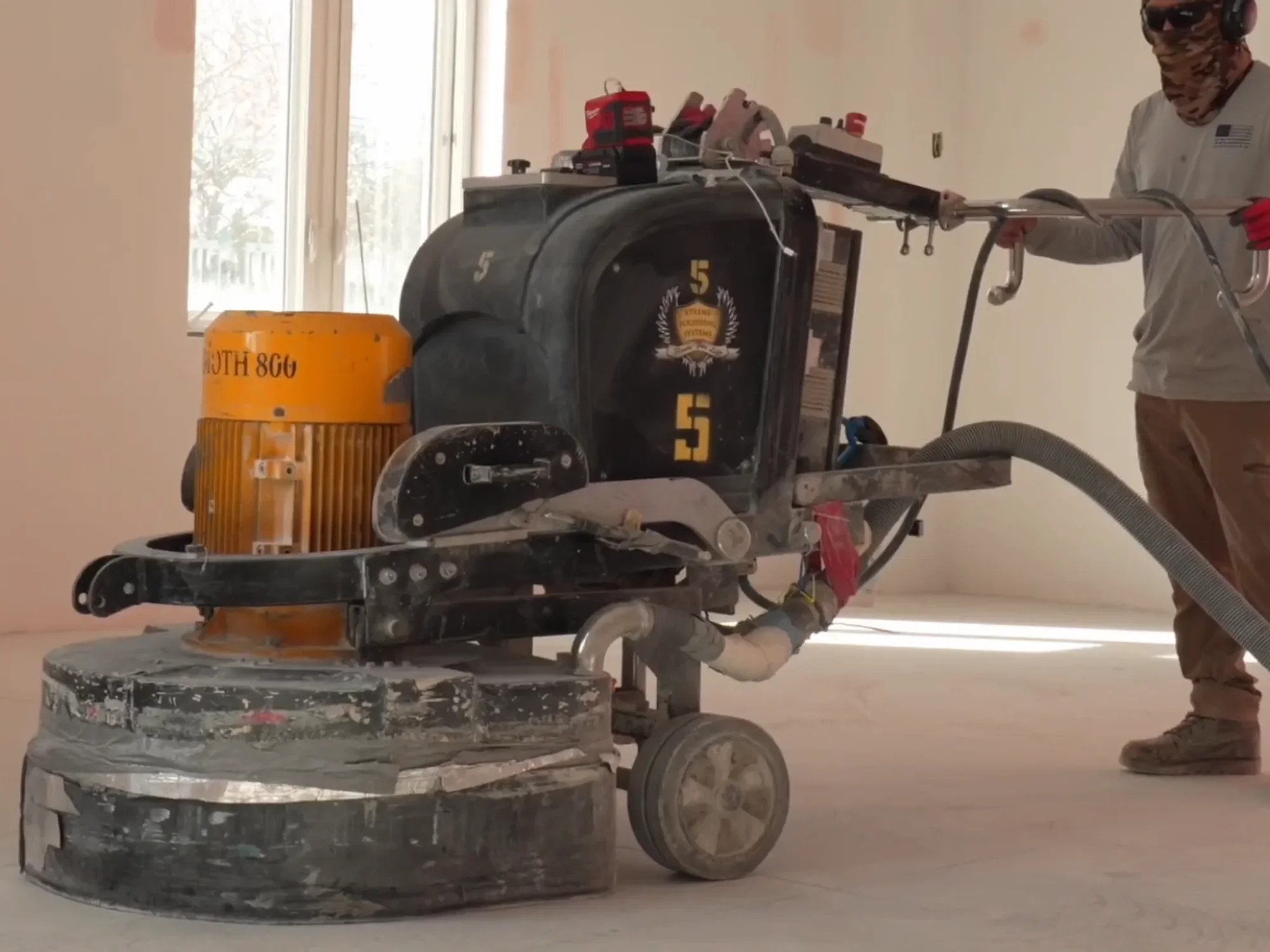 Crew member running a floor grinder with its dust extraction hose and vacuum